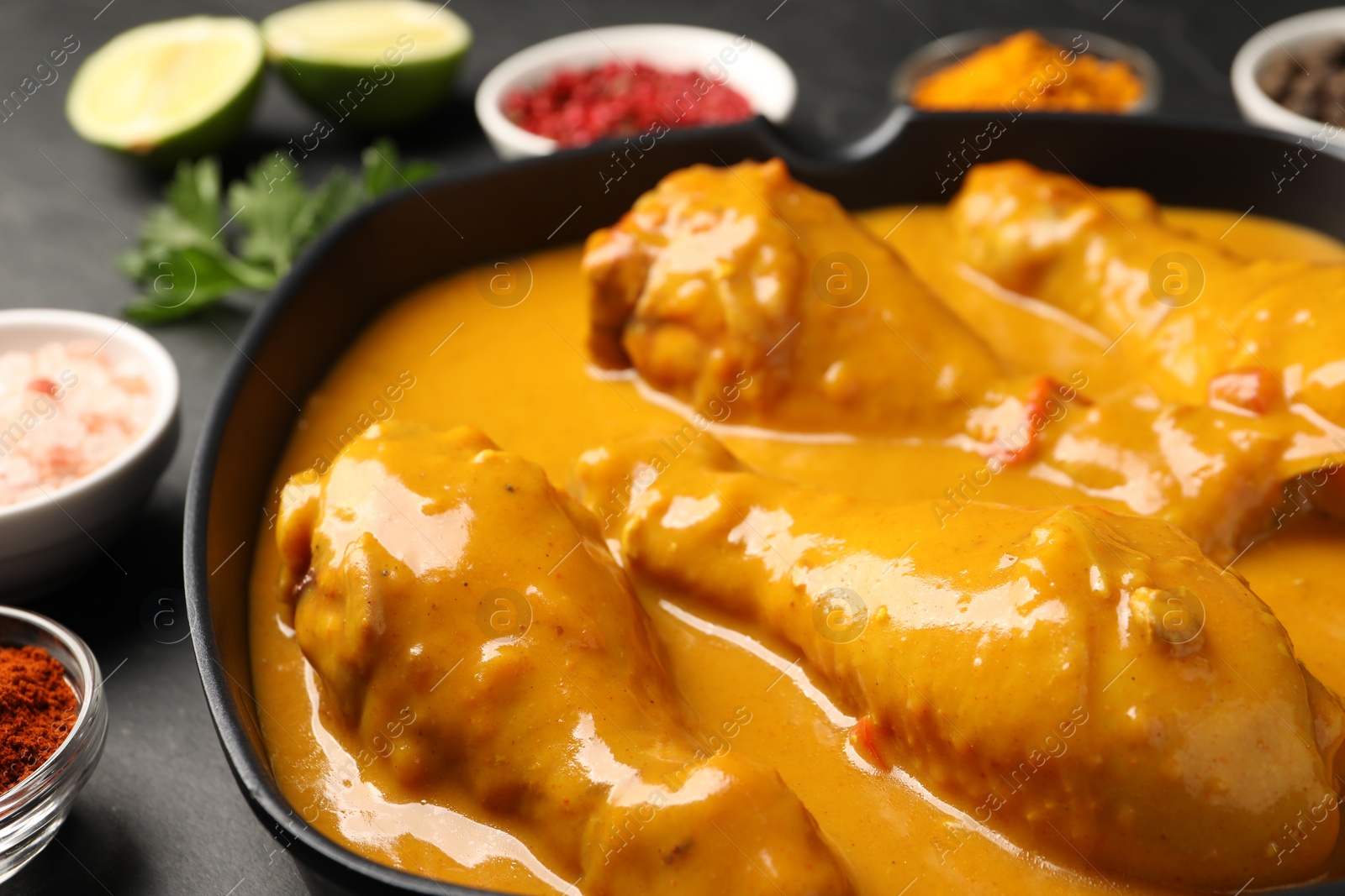 Photo of Tasty chicken curry and ingredients on black table, closeup