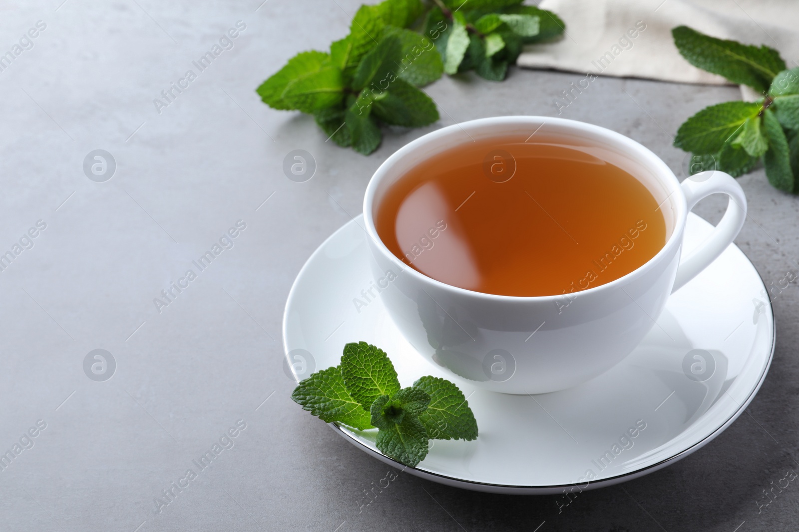 Photo of Cup of hot aromatic mint tea on light grey table. Space for text