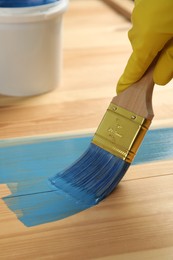 Worker applying blue paint onto wooden surface, closeup