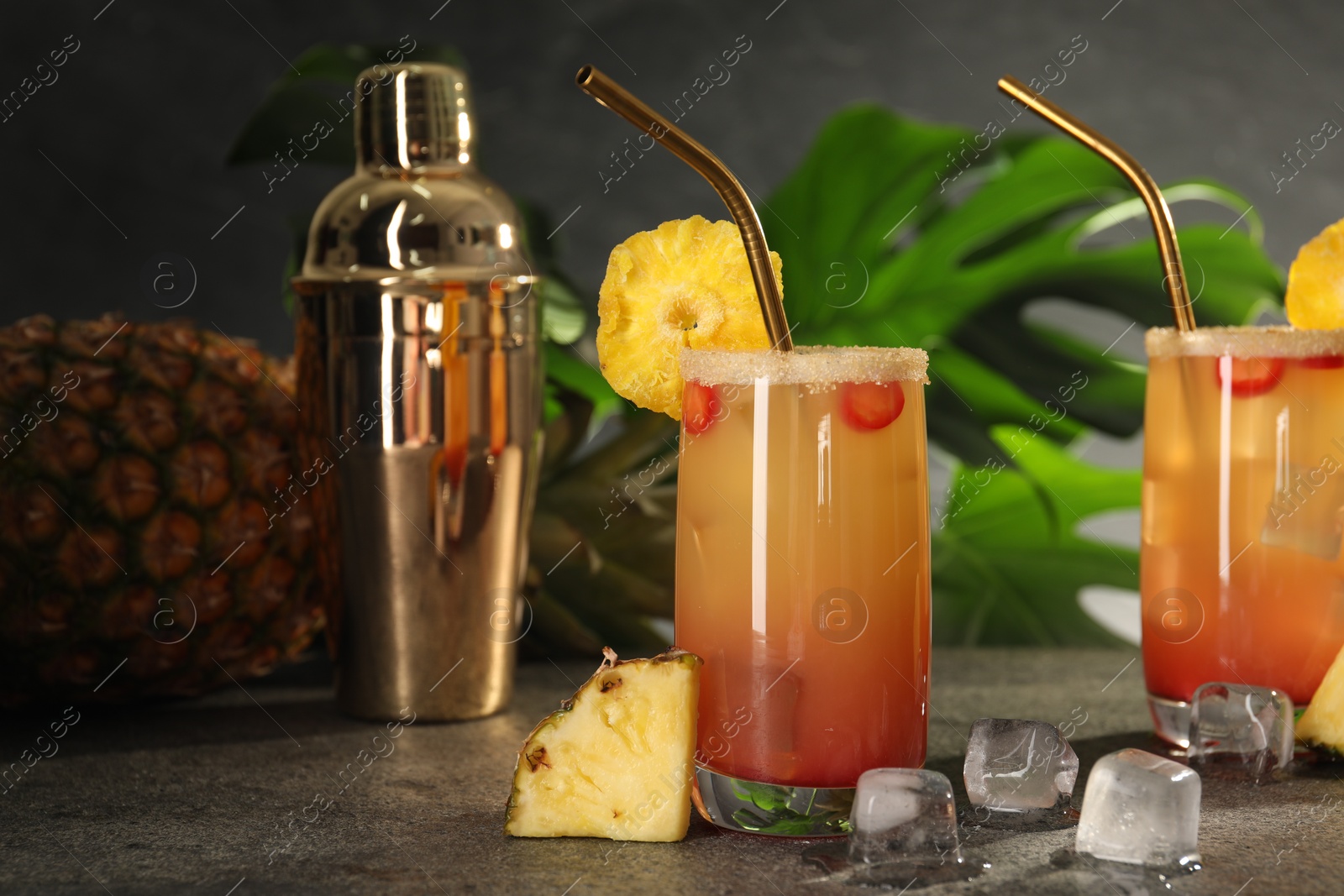 Photo of Glasses of tasty pineapple cocktail, sliced fruit and ice cubes on grey table. Space for text