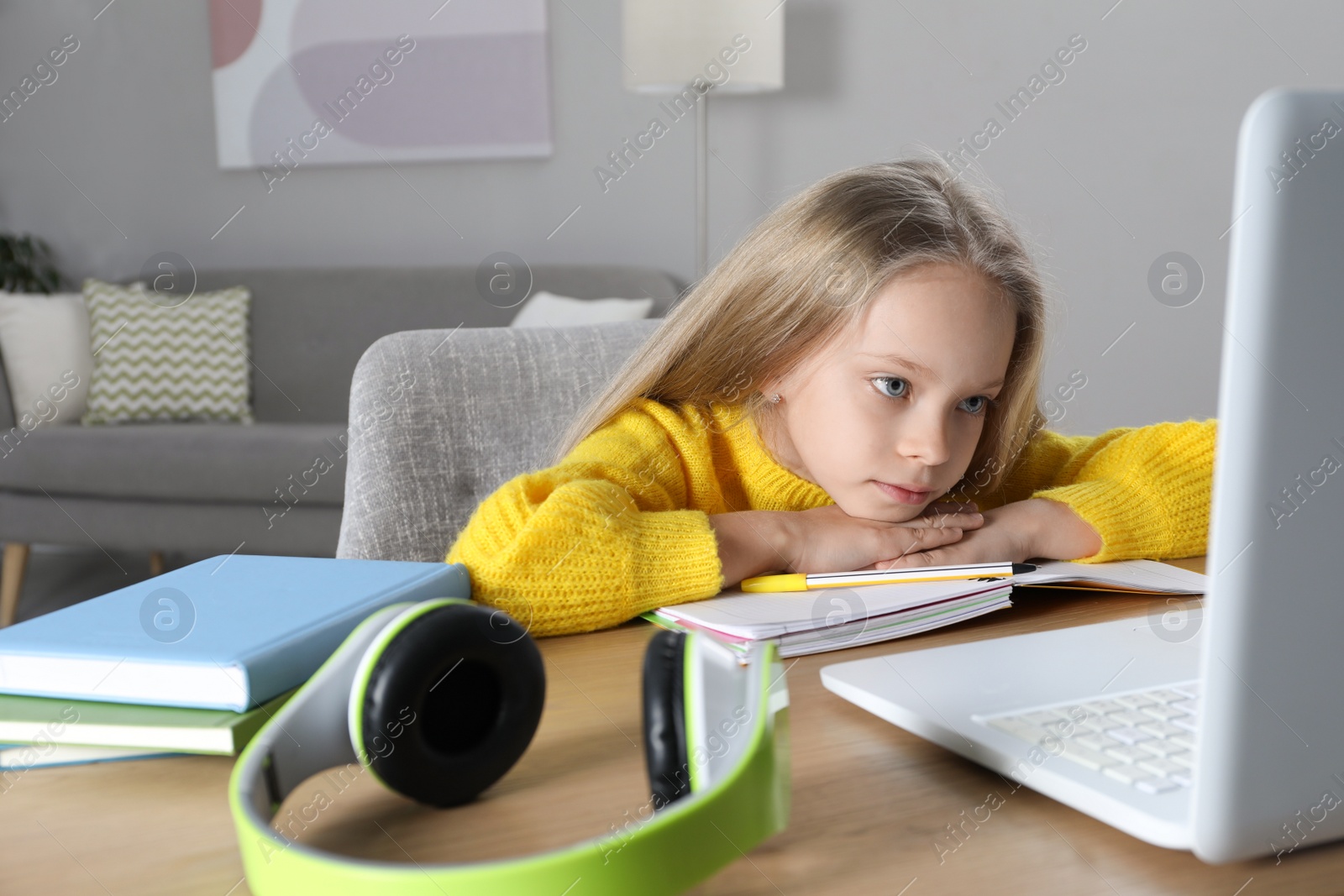 Photo of Cute little girl with modern laptop studying online at home. E-learning