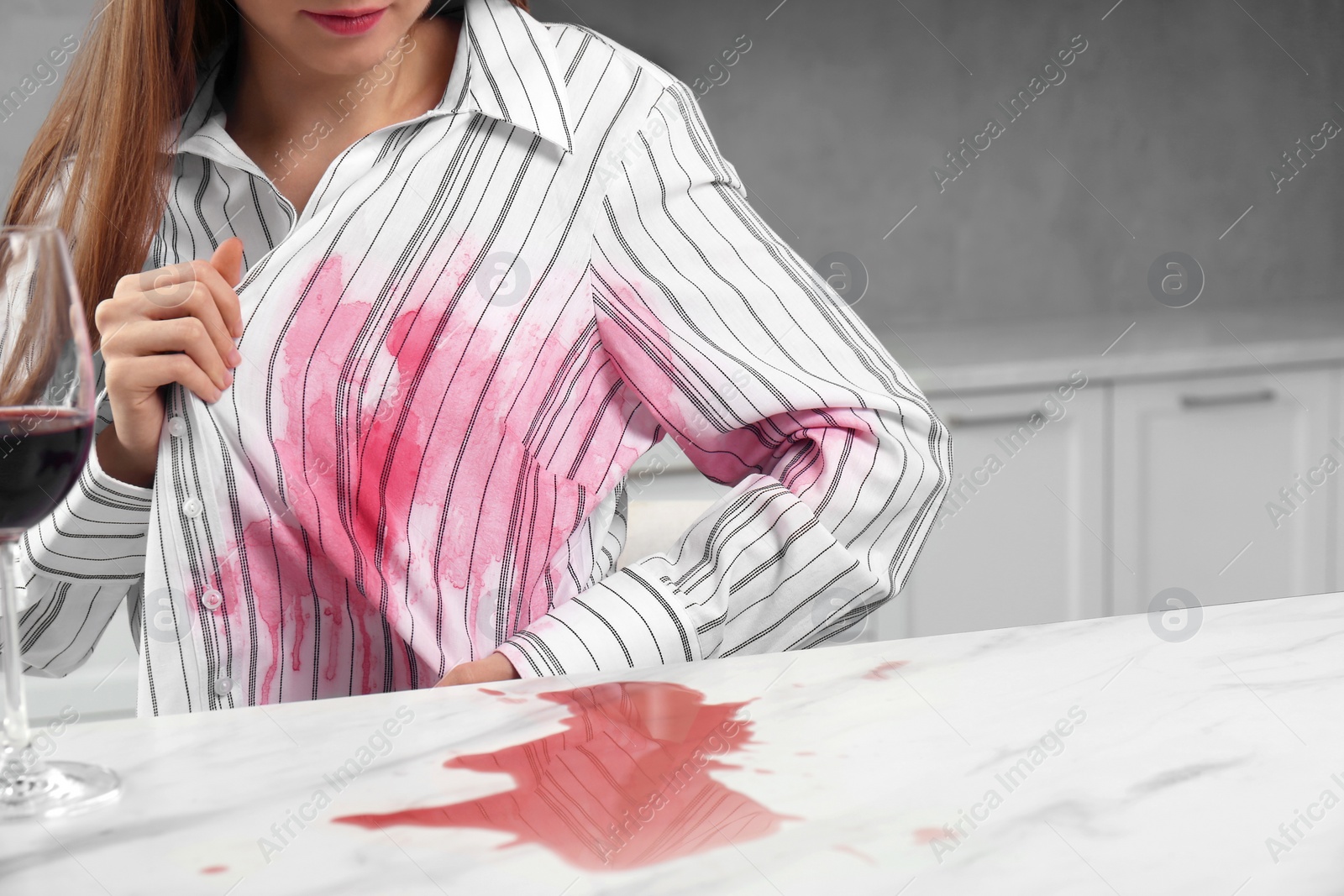Photo of Woman with spilled wine over her shirt and marble table in kitchen, closeup