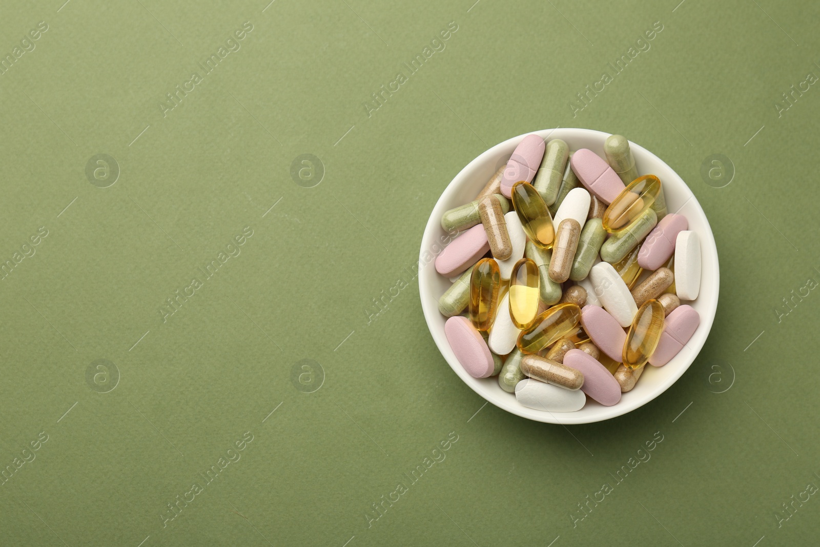 Photo of Different vitamin pills in bowl on olive background, top view. Space for text