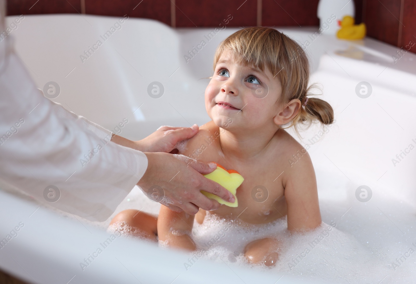 Photo of Mother washing her little daughter with sponge in bathtub, closeup