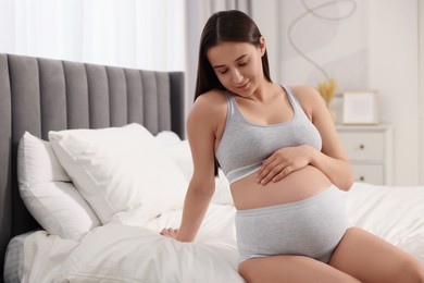 Photo of Beautiful pregnant woman in comfortable maternity underwear on bed at home
