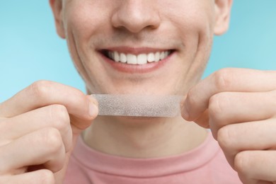 Photo of Young man with whitening strip on light blue background, closeup