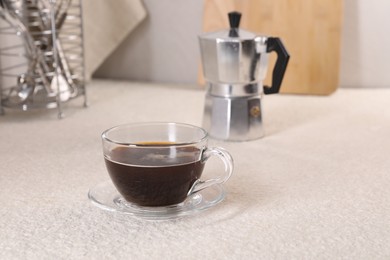 Delicious coffee in cup and moka pot on light textured table