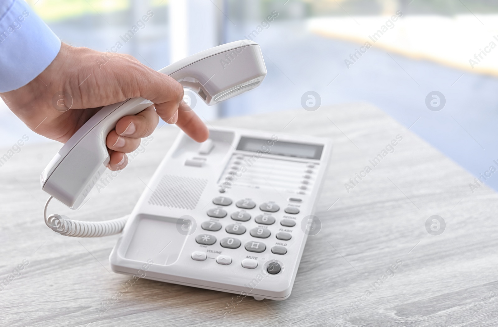 Photo of Man dialing number on telephone at table indoors