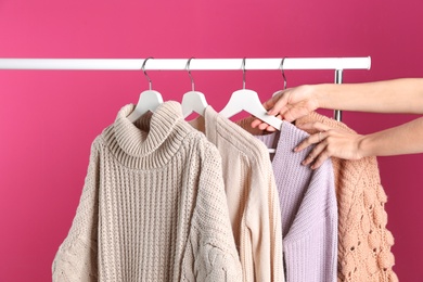 Woman choosing sweater on rack against color background