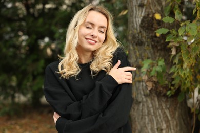 Photo of Happy woman in stylish warm sweater near tree outdoors