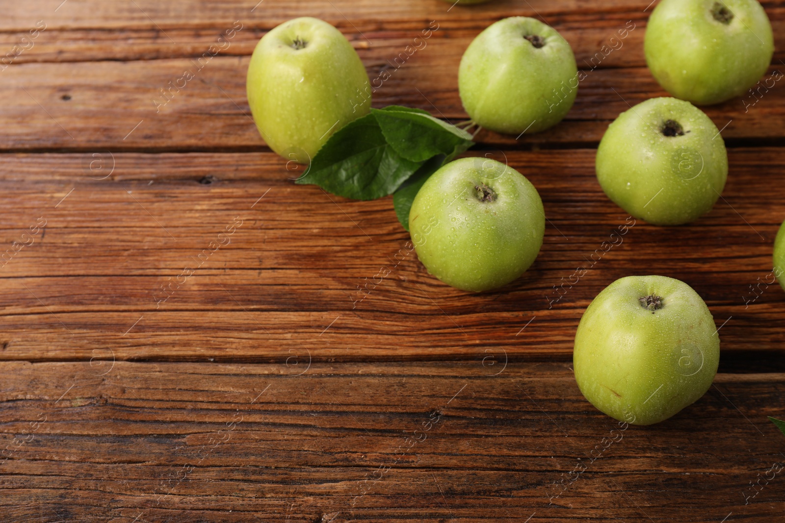 Photo of Fresh ripe green apples with water drops on wooden table. Space for text