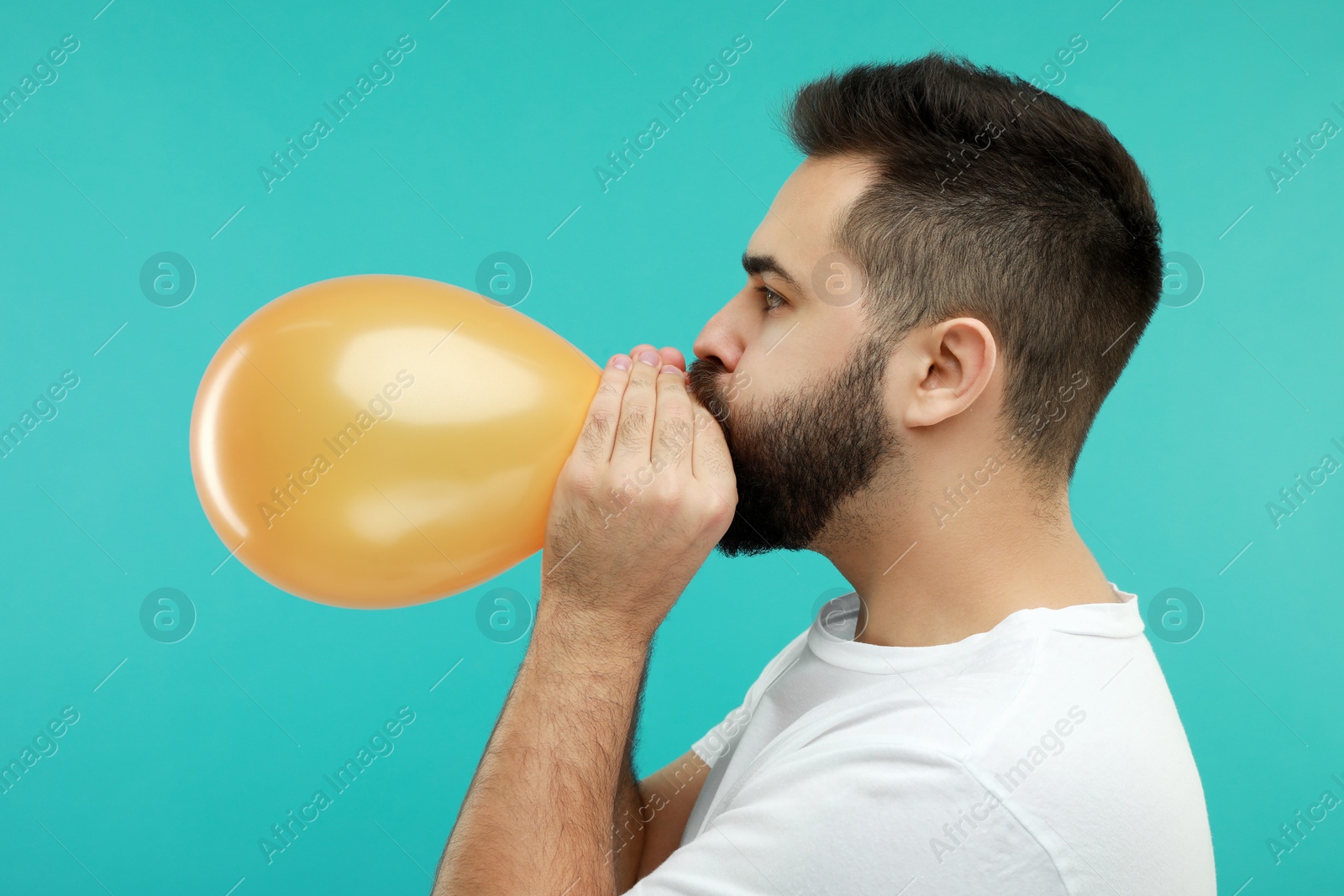 Photo of Man inflating bright balloon on turquoise background