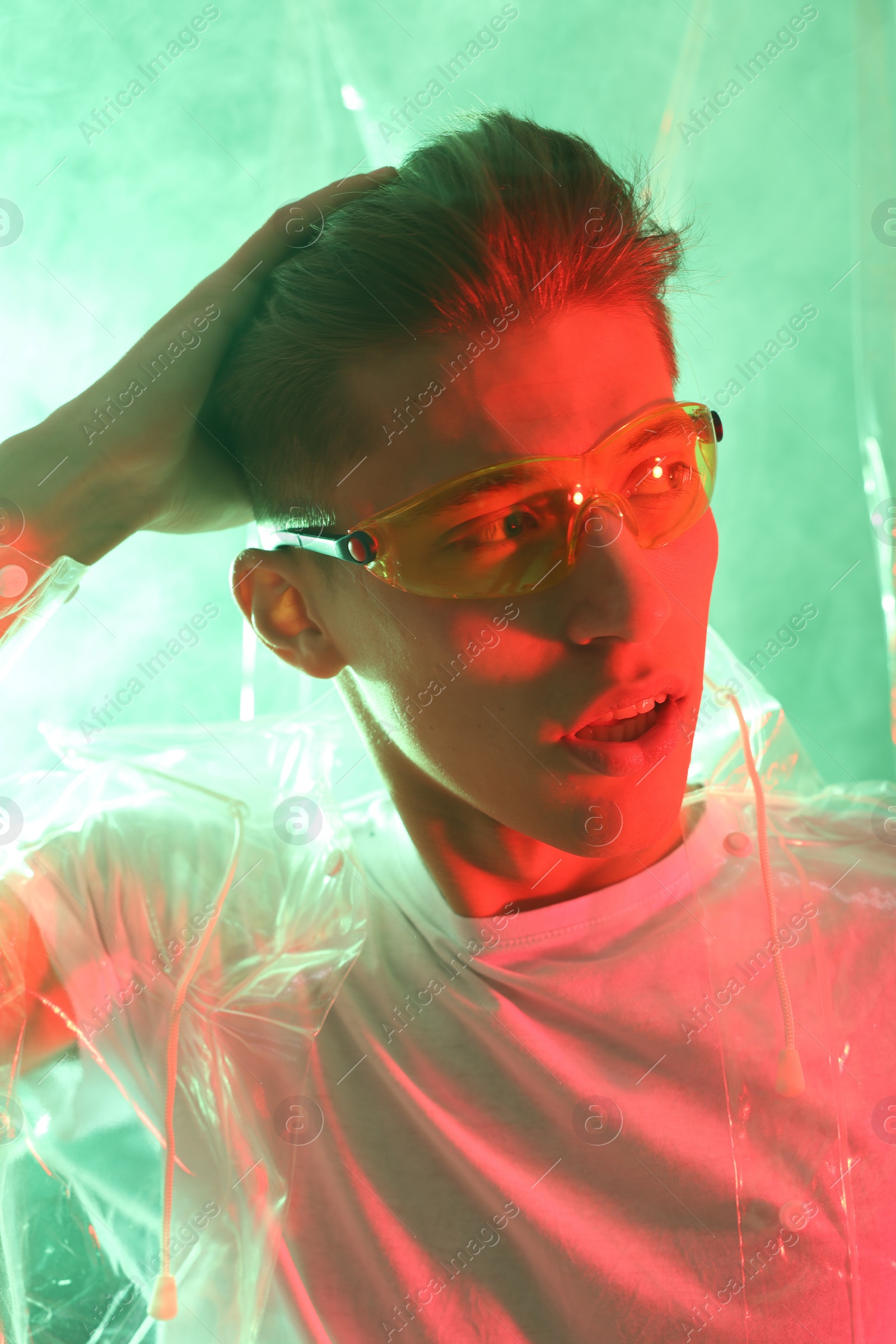 Photo of Stylish young man wearing clear coat and glasses in neon lights