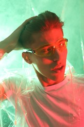 Stylish young man wearing clear coat and glasses in neon lights