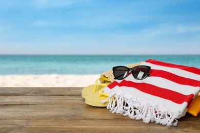Beach bag with towel, flip flops and sunglasses on wooden surface near seashore. Space for text