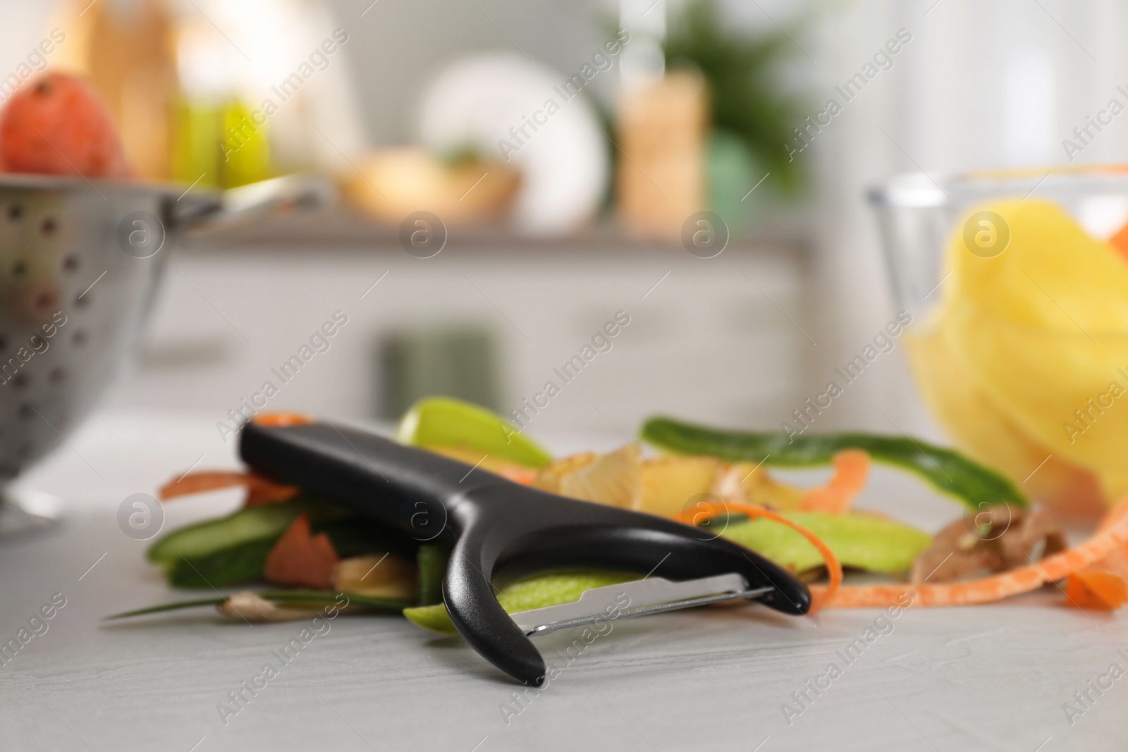 Photo of Peels of fresh vegetables and peeler on white table, closeup