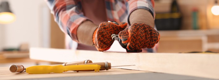Carpenter shaping wooden bar with plane at table in workshop, focus on hands. Banner design