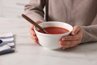 Photo of Woman eating tasty tomato soup at white marble table, closeup