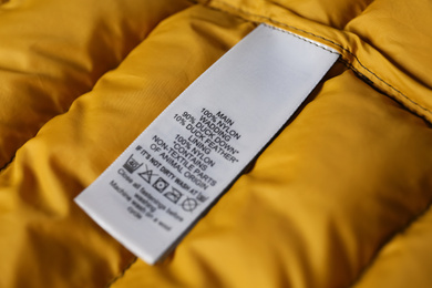 Photo of Clothing label with care symbols and material content on yellow jacket, closeup view
