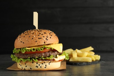 Photo of Burger with delicious patty and french fries on gray table against dark background, space for text
