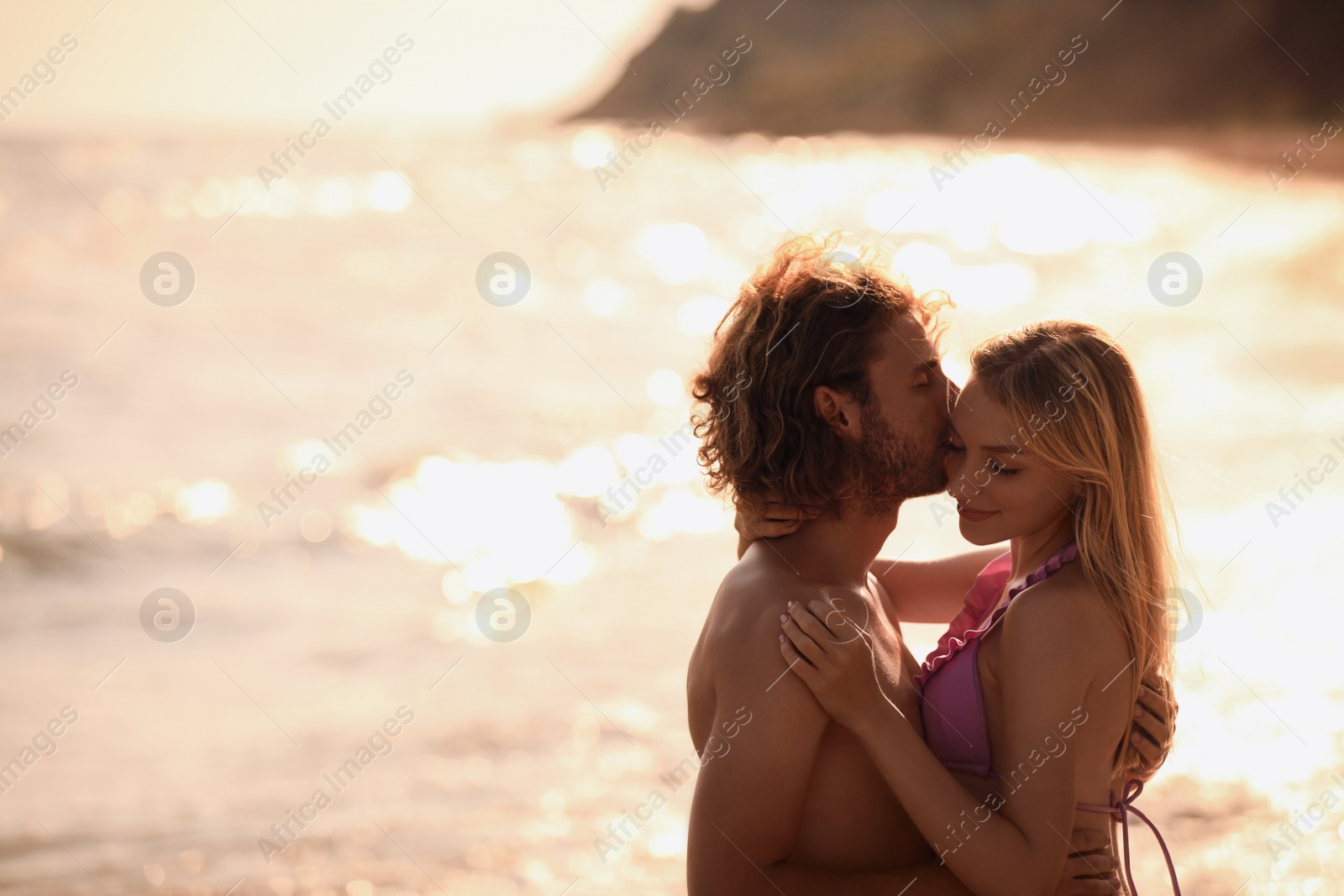 Photo of Young woman in bikini kissing her boyfriend on beach at sunset. Lovely couple