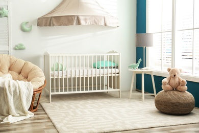 Photo of Cute nursery interior with comfortable crib near white wall