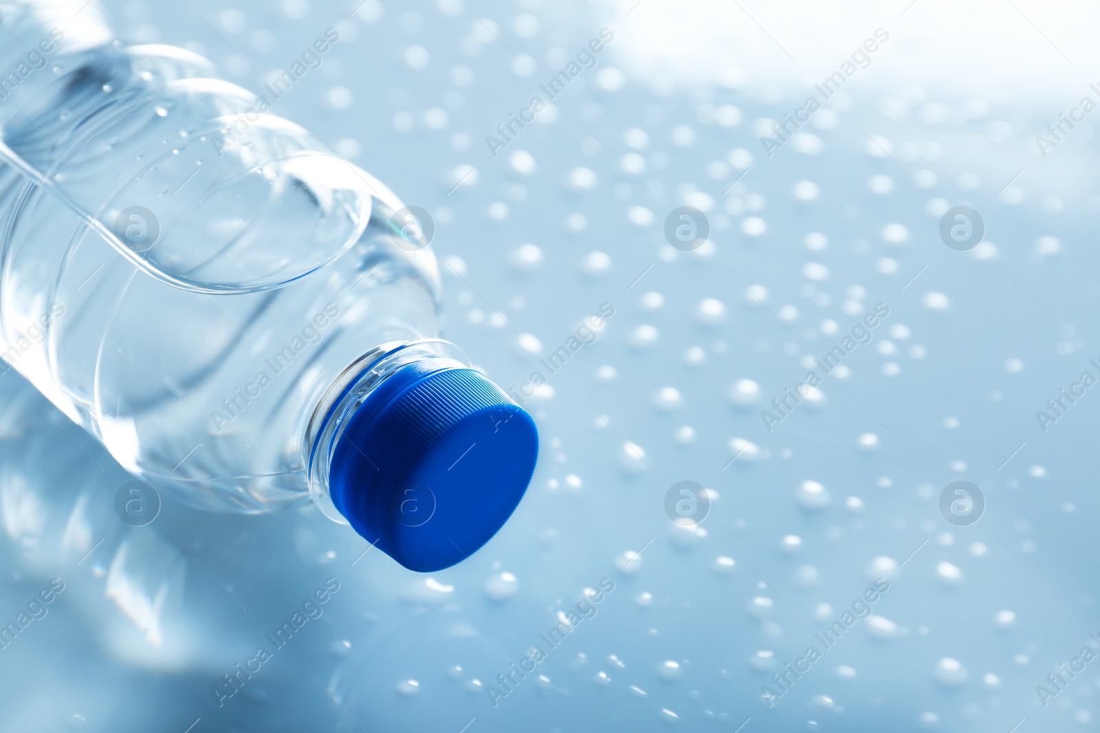 Photo of Bottle of water on wet light surface, closeup. Space for text