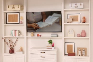 Photo of TV and shelves with different decor in room. Interior design