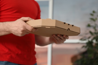 Courier with pizza box on blurred background, closeup