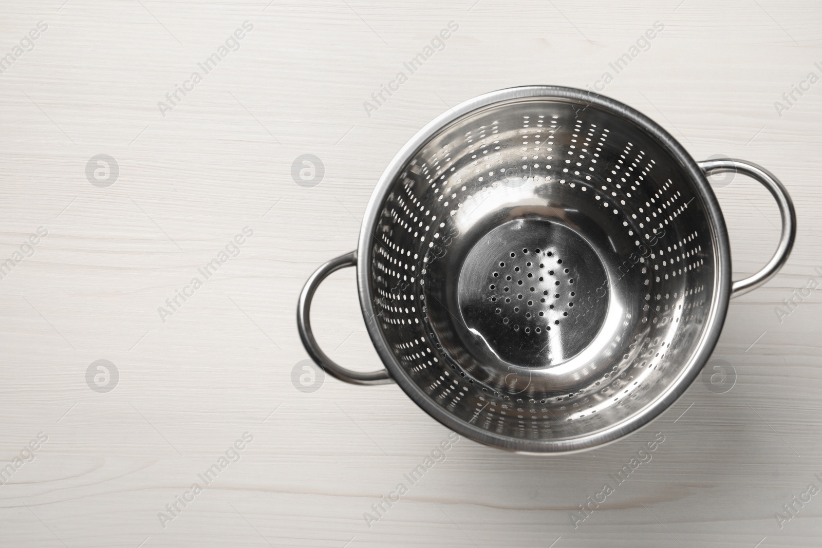 Photo of Metal colander on white wooden table, top view. Space for text