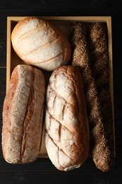 Photo of Basket with different types of fresh bread on black wooden table, top view