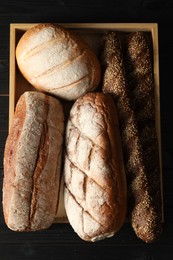 Basket with different types of fresh bread on black wooden table, top view