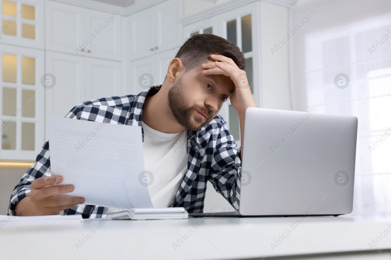 Photo of Man with laptop doing taxes at table in kitchen