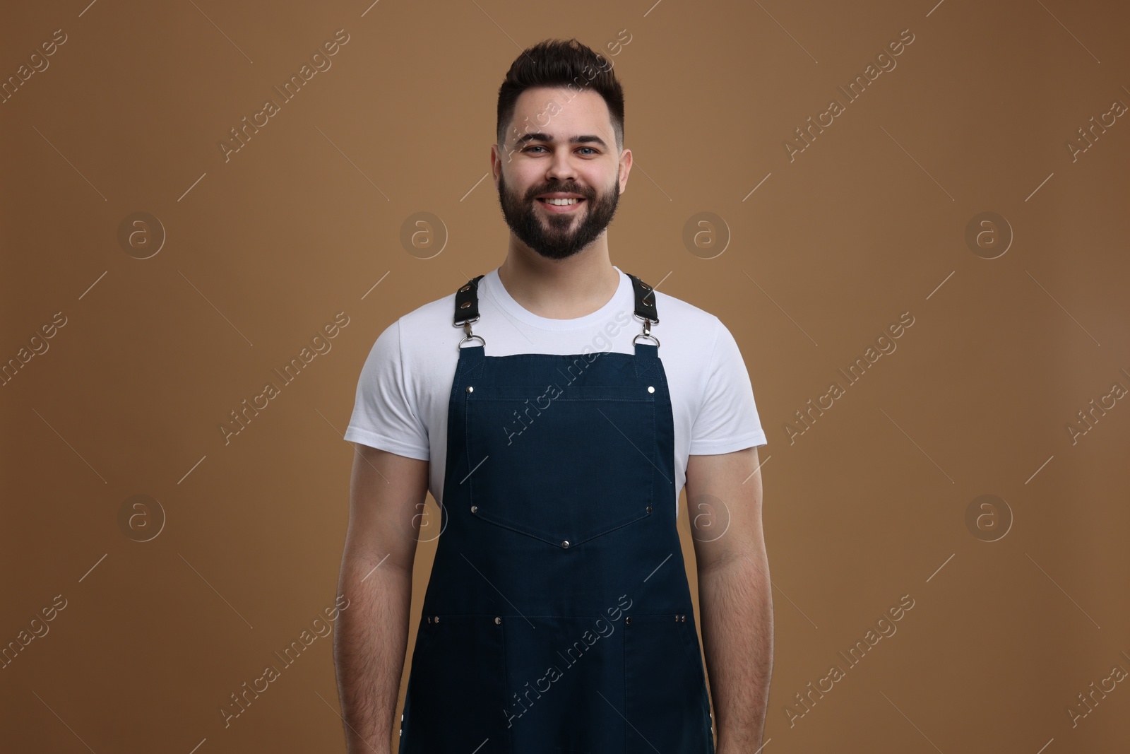 Photo of Smiling man in kitchen apron on brown background. Mockup for design