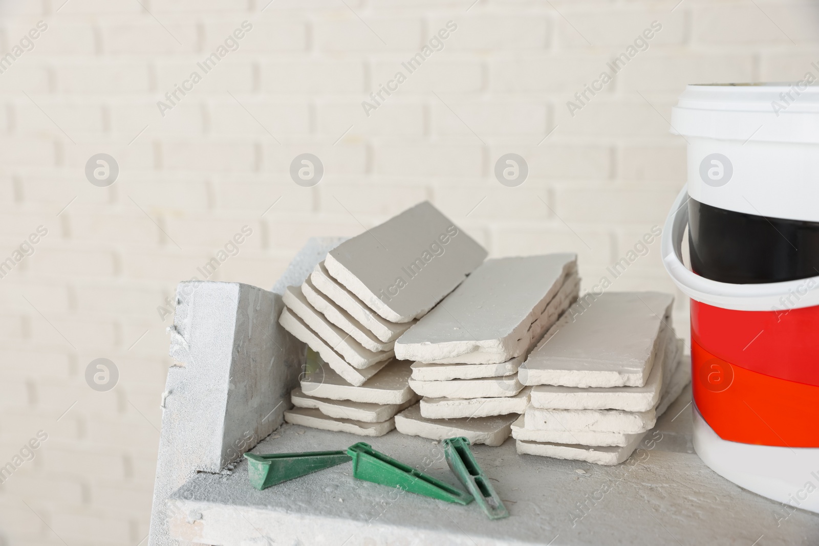 Photo of Bucket with cement, tile spacers and many white decorative bricks in room