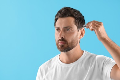 Handsome man applying cosmetic serum onto his face on light blue background. Space for text