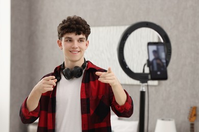 Smiling teenage blogger pointing at his smartphone while streaming at home