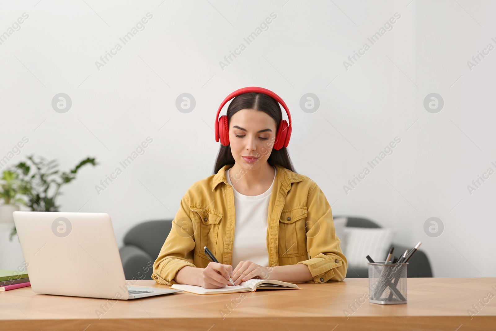 Photo of Online translation course. Student in headphones writing near laptop at home