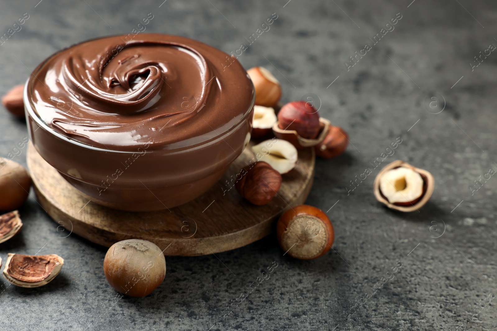 Photo of Glass bowl with tasty chocolate hazelnut spread and nuts on grey table