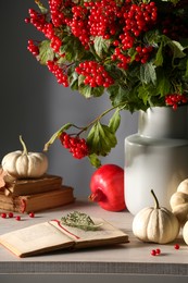 Photo of Composition with ripe red viburnum berries, books and pumpkins on table. Cozy autumn atmosphere