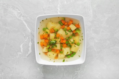 Bowl of fresh homemade vegetable soup on grey marble background, top view