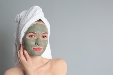 Photo of Young woman with clay mask on her face against grey background, space for text. Skin care