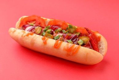 Tasty hot dog with onion, tomato, pickles and sauce on red background, closeup