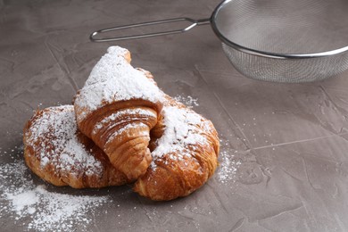 Tasty croissants with sugar powder and sieve on grey textured table, closeup