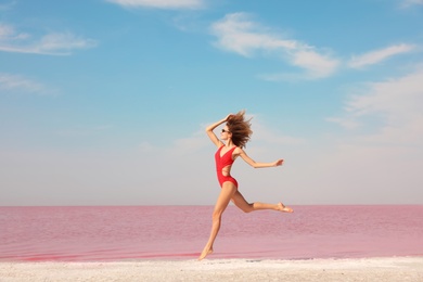 Beautiful woman in swimsuit jumping near pink lake on sunny day