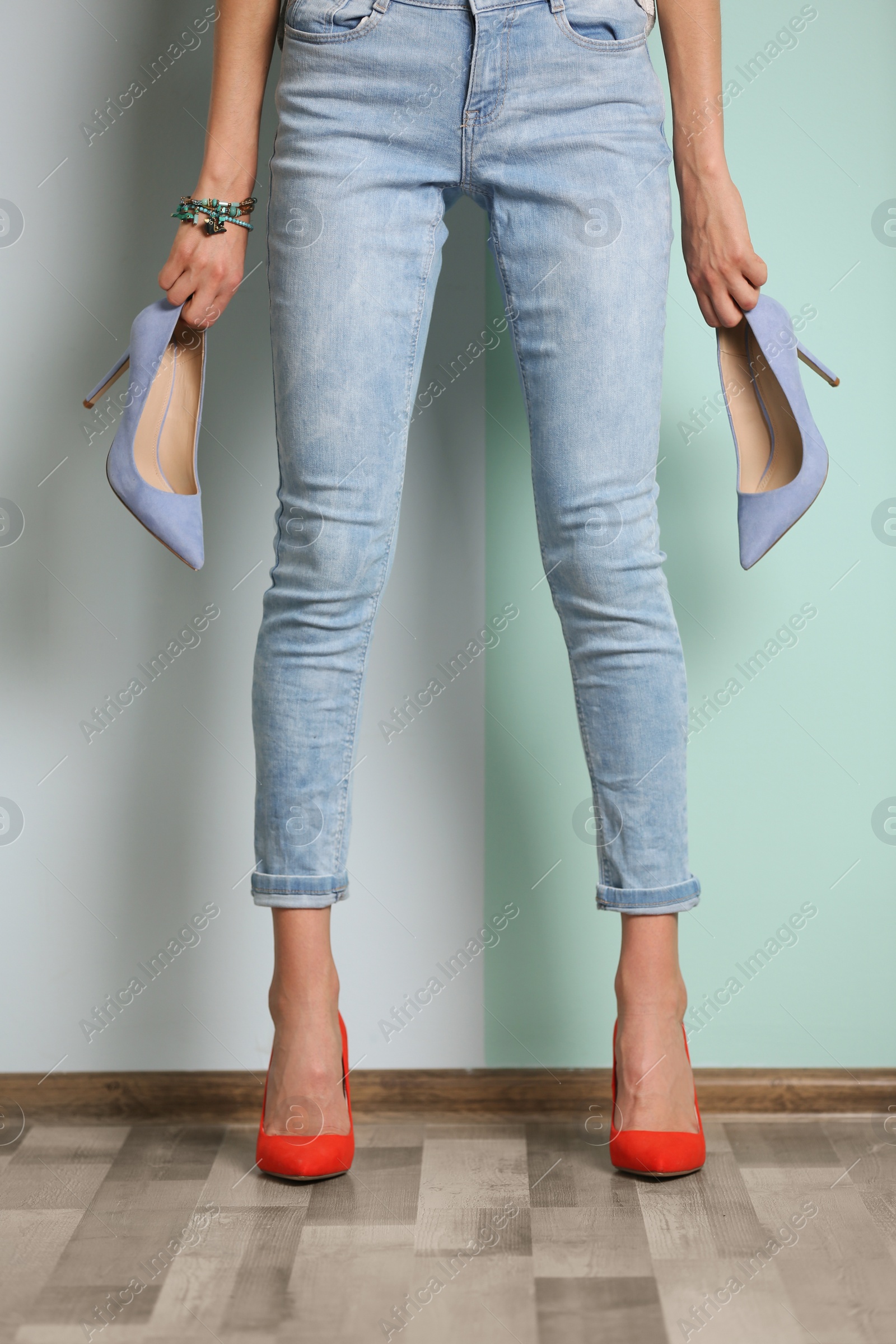 Photo of Young woman with different high heeled shoes near color wall, closeup