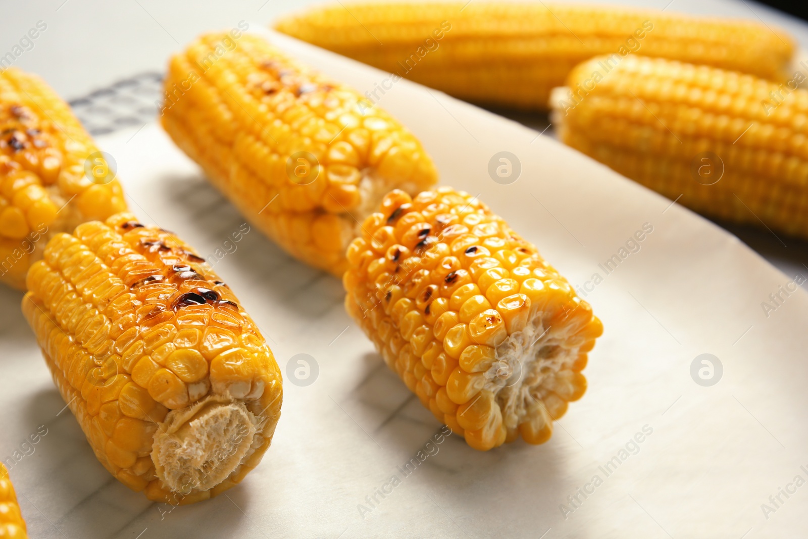 Photo of Fresh grilled tasty corn cobs on parchment paper, closeup