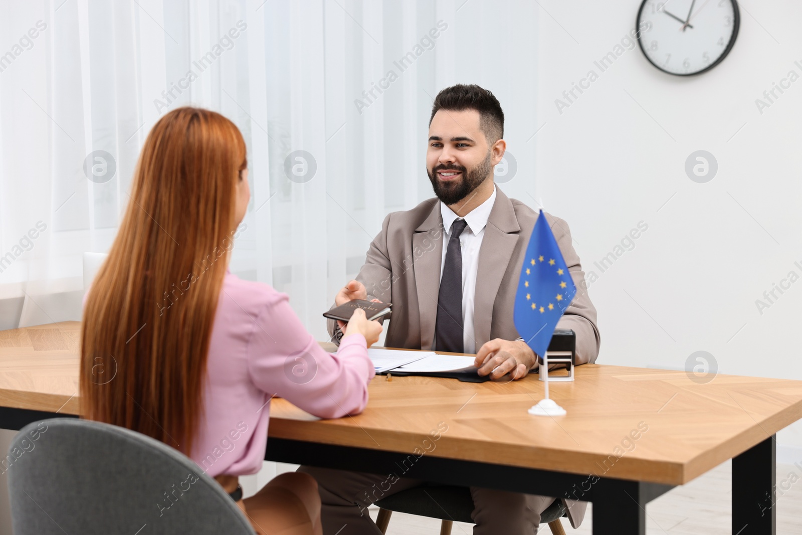 Photo of Immigration to European Union. Woman giving her passport to smiling worker in embassy