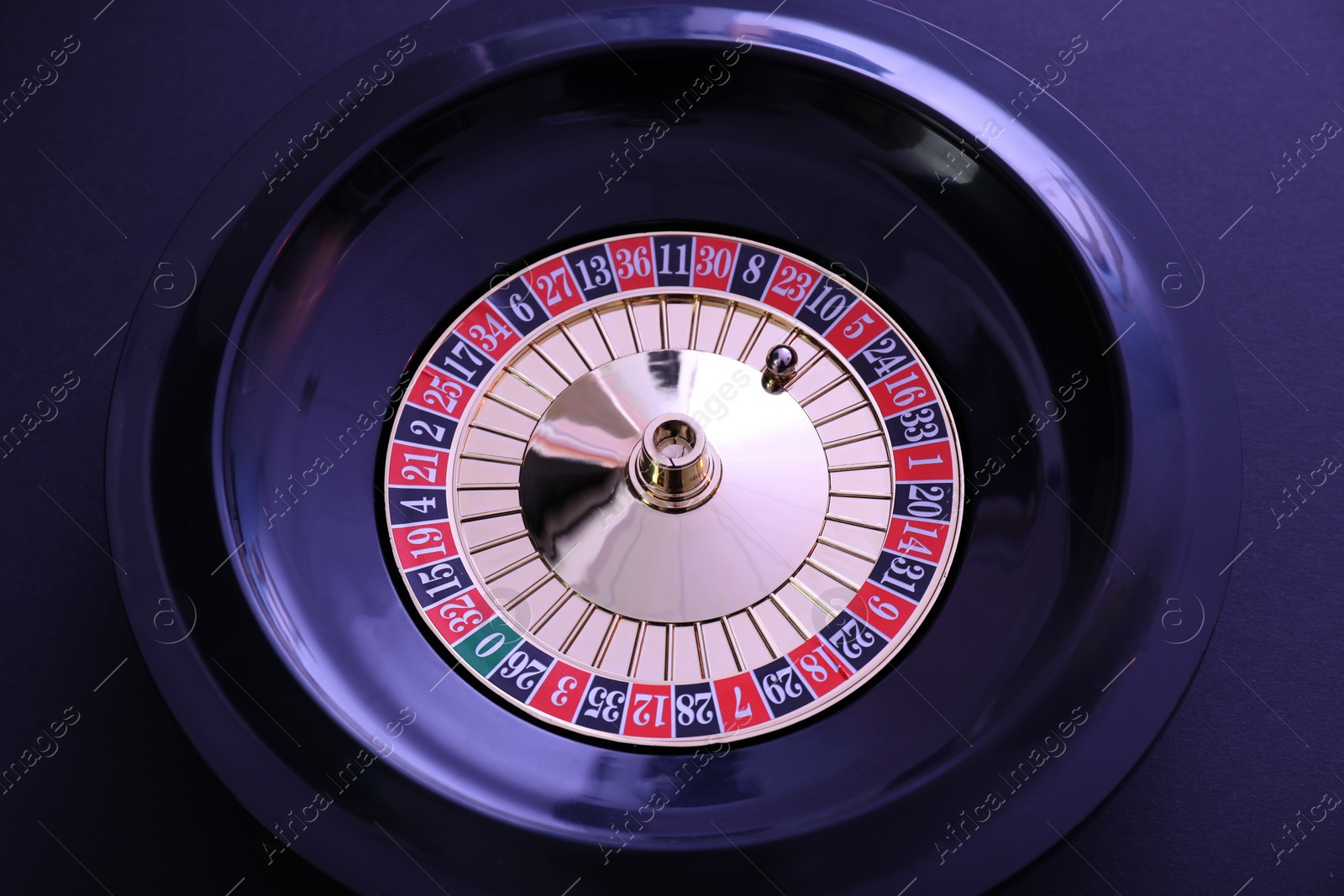 Photo of Roulette wheel with ball on dark violet background, top view. Casino game