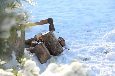 Photo of Metal axe in wooden log and pile of wood outdoors on sunny winter day. Space for text